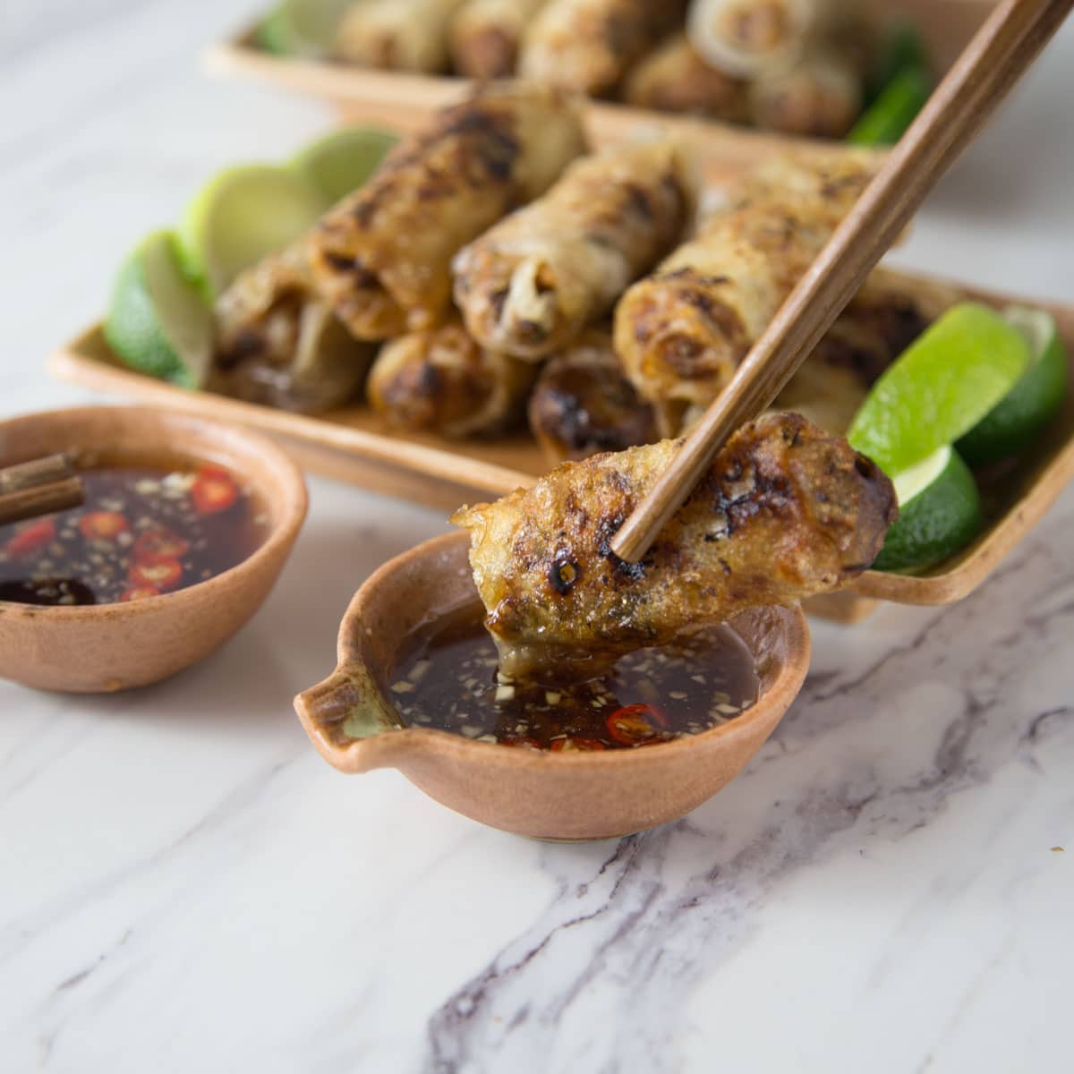 A pair of chop sticks dipping a fried spring roll into nuoc cham.