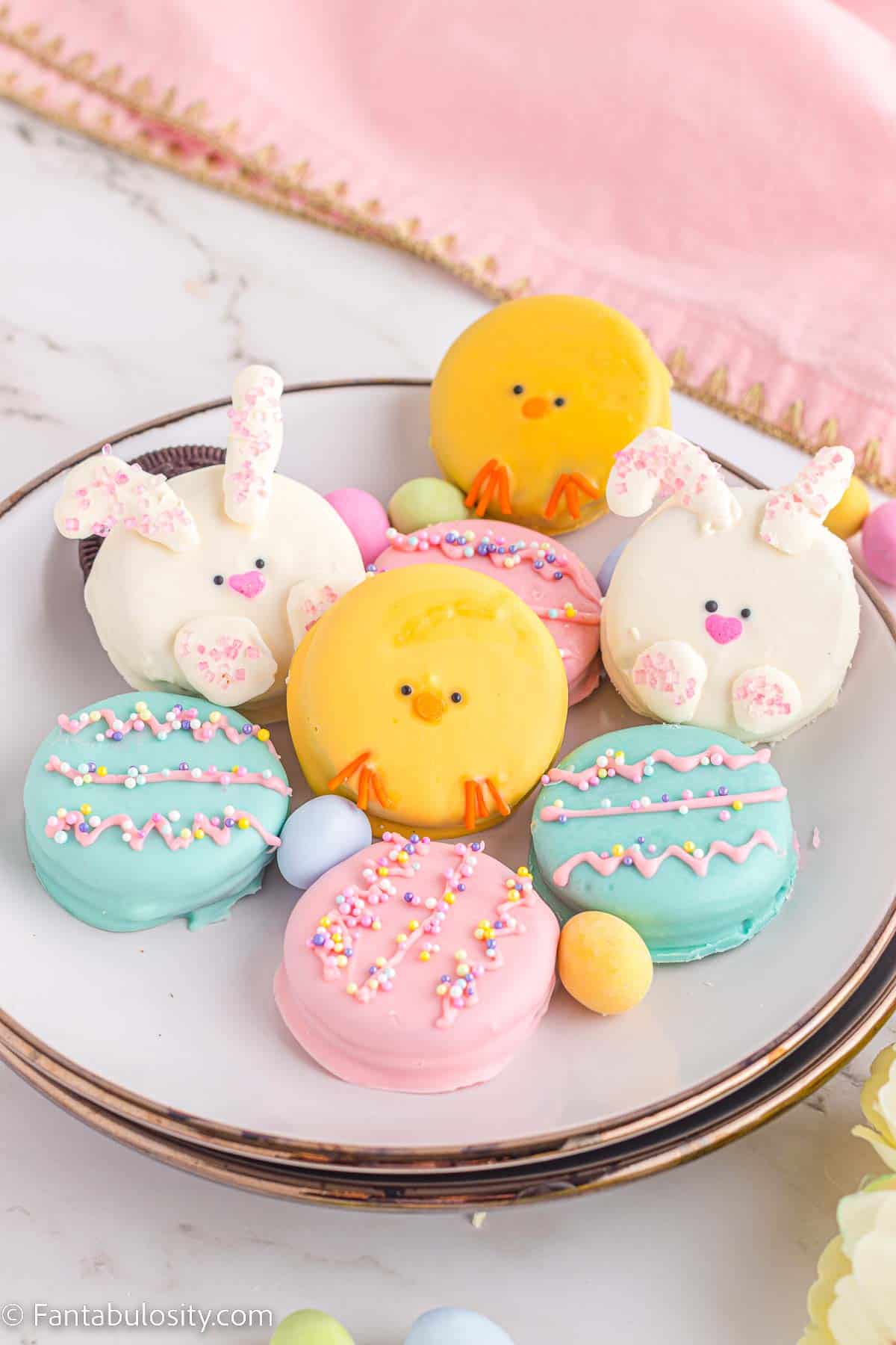 Easter Oreos that are decorated like eggs, bunnies and chicks, sitting on white plate.