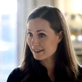 A woman, Prime Minister Sanna Marin, looks at someone outside the frame of the photo and half-smiles.