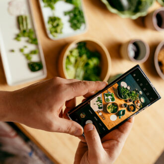 Unas manos sostienen un teléfono móvil mientras hacen una foto de una mesa servida con varios cuencos de verduras.