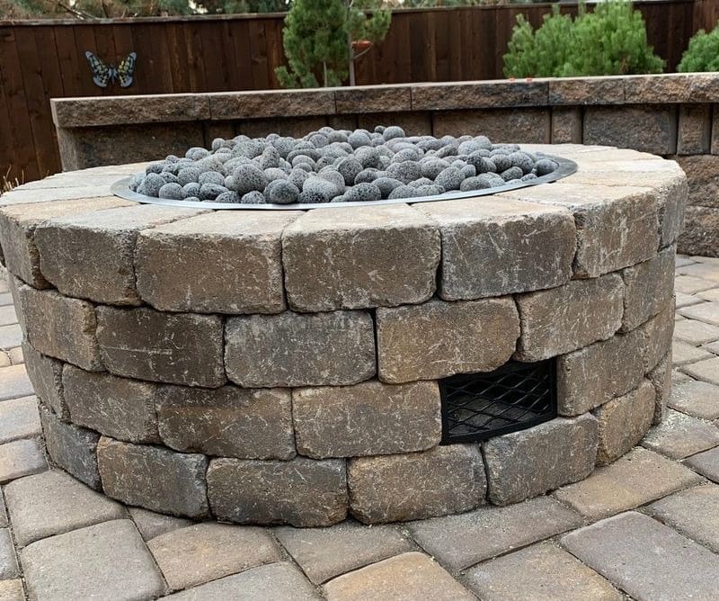 A fire pit with stones in it sitting on top of a brick patio.