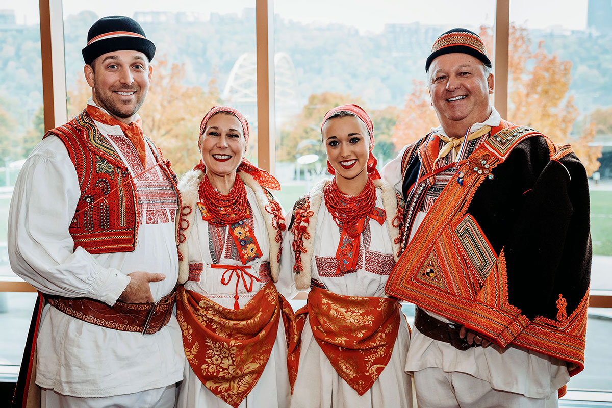 A family of four, including adult daughter and son, pose arm in arm wearing traditional Croatian costume.