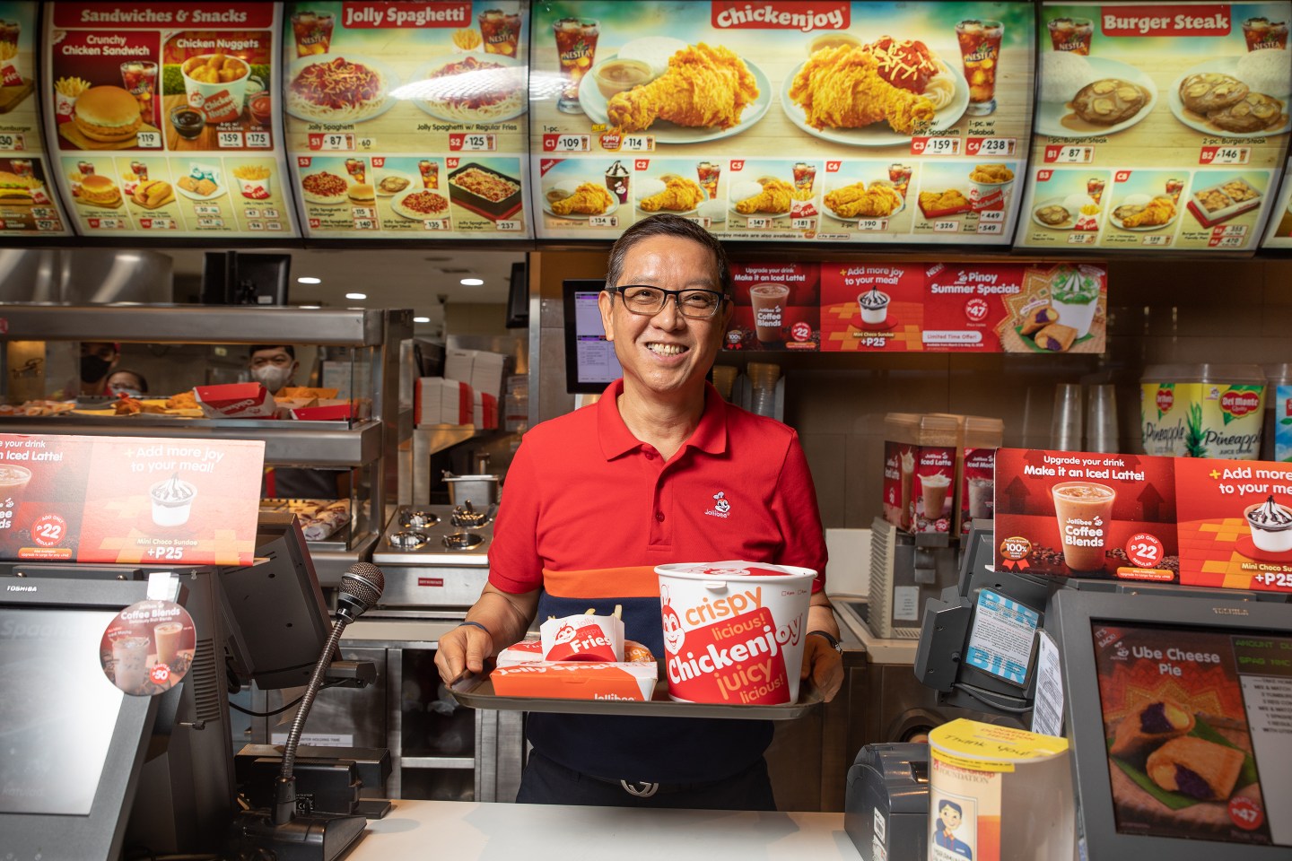 Jollibee CEO Ernesto Tanmantiong behind the counter holding a tray of Chickenjoy and fries.