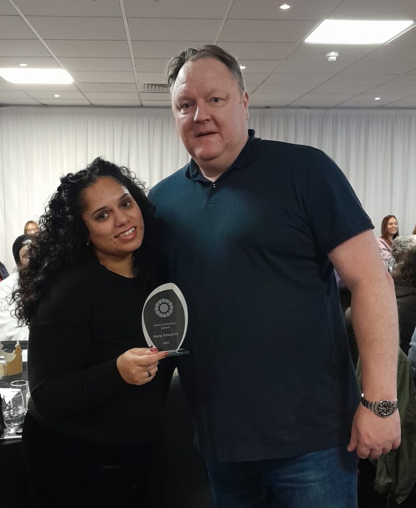 Two people smile toward the camera with one holding a glass award for the Great Leadership Award at the 2023 Gordon Moody Staff Awards.