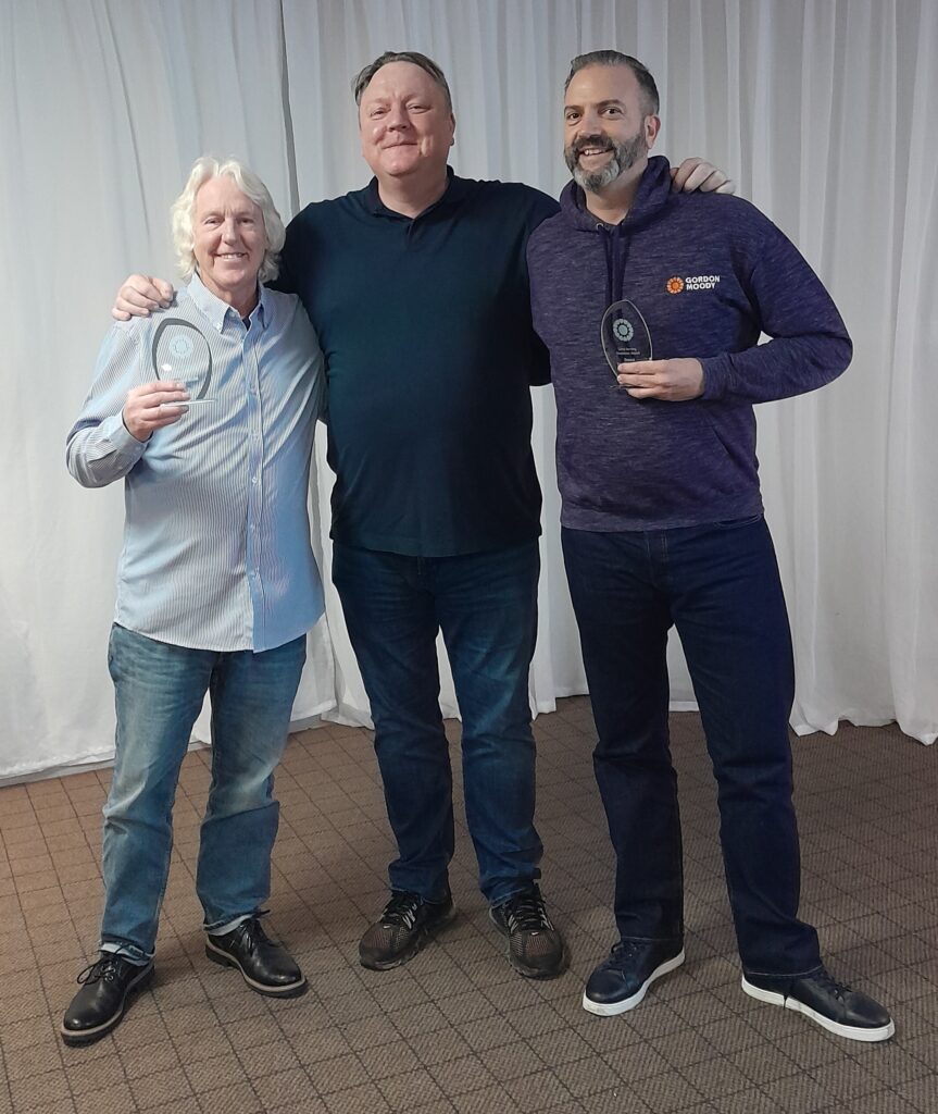 Three people smile toward the camera with two people both holding a glass award for the Long Serving Employee Award at the 2023 Gordon Moody Staff Awards.