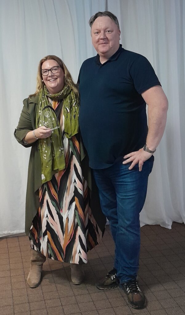 Two people smile toward the camera with one holding a glass award for the Ray of Sunshine Award at the 2023 Gordon Moody Staff Awards.