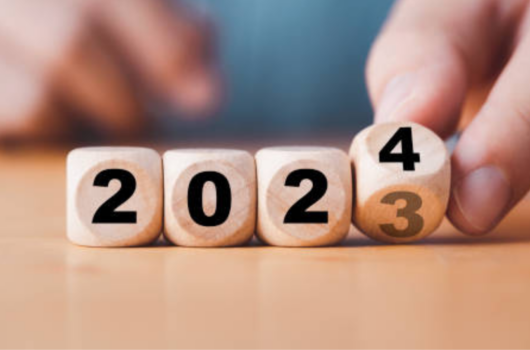 An image of dice showing the date 2023 changing to read 2024 by a person wearing a blue top.