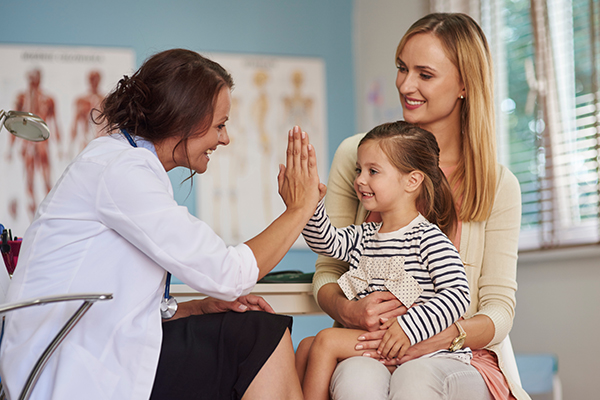 A pediatrician giving a high-five to a young girl, with the mother smiling beside them.