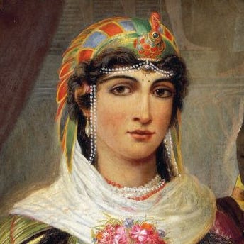 cleopatra vii wears a colorful head piece, pearl jewelry and a white scarf with a floral bouquet in front of her chest