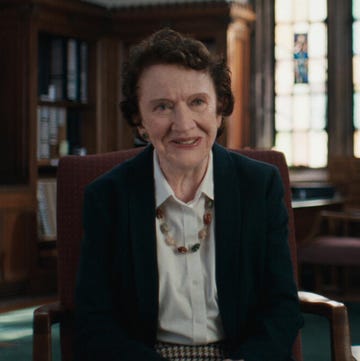 dr ann burgess sitting in a chair with book shelves and windows in the background of a study area