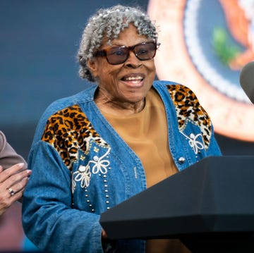 opal lee, wearing a denim designed coat, yellow shirt, and sunglasses, speaks at a podium with two microphones and the us presidential seal, standing next to a laughing kamala harris