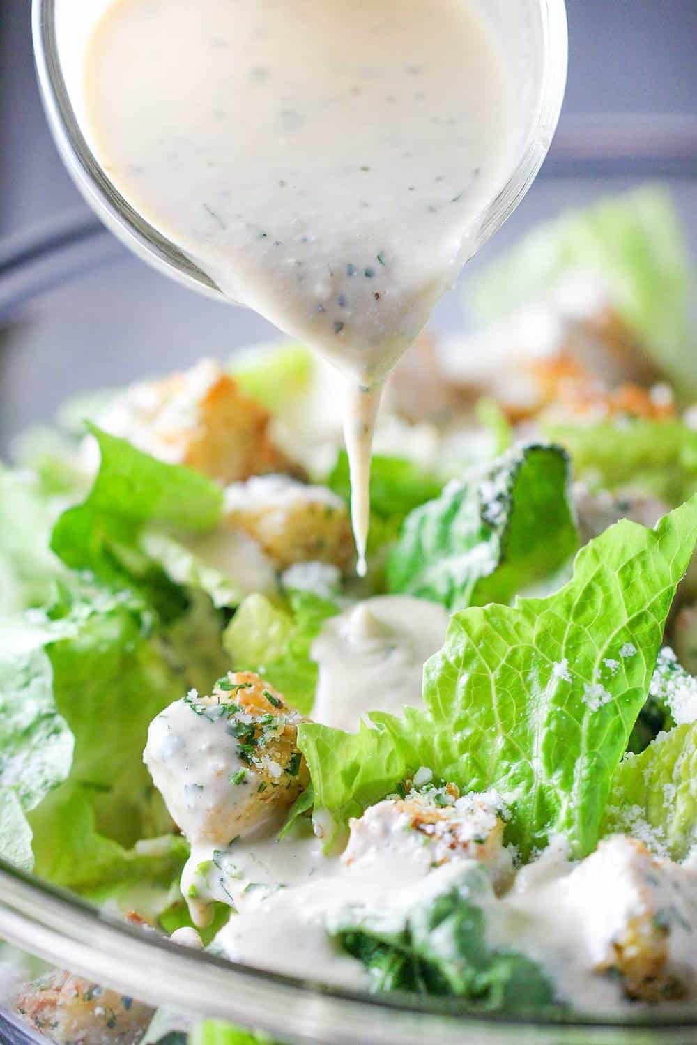 A small pitcher pouring dressing onto a classic Caesar salad.