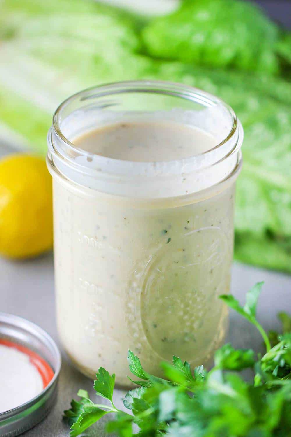 A mason jar holding Caesar dressing with lettuce and a lemon nearby. 