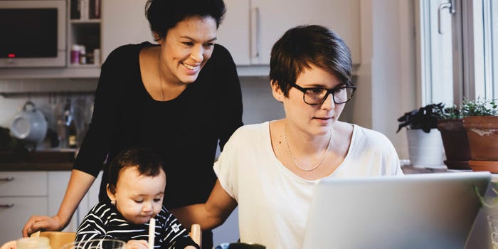 Two women look at a laptop while their child sits next to them