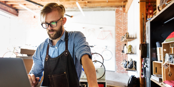 A photo of a bicycle shop owner working on a laptop at a workbench.