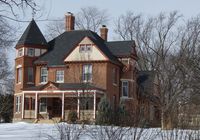 The George W. Baird House in Edina, Minnesota, built in 1886 by a prominent farmer in the Edina Mills community, is two stories tall & is built in the Eastlake style. It has a distinctive silhouette, with multiple roof shapes, dormers, a square tower, & tall brick chimneys. The large front porch has wooden posts & balusters, with a pediment over the entrance. The exterior is embellished with stone window trim, transoms, scalloped wooden shingles in the gables, & belt courses.