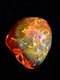 "This substantial 11 ct. Mexican Fire Opal is dome or blister shaped. The word blister may not seem like an attractive adjective but it is an apt description of for many organic shaped Mexican Fire Opals. This vibrant stone morphs from a deep orange color into gold with flashes of iridescent gold and green. The stone is nicely symmetrical and 3/4\" at it's widest point.  This opal is available on it's own or you may contact me to create a one a kind design using this stone.  All Marty Magic Jewelry is packaged in a beautiful box, embossed with the gold foil Marty Magic dragon logo. Perfect for any occasion! Mined in Mexico"