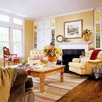 Sunny Living This color palette warms in any season. Walls in pale gold bring out the wood tones in the flooring. Against this buttery backdrop, we notice accents of red in one chair, several pillows, and an area rug.