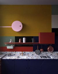 13 a dark blue kitchen with a terrazzo countertopp, brass fixtures and postal red shelf plus green and yellow color blocking - DigsDigs