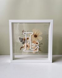 "Our pressed flower frame - bloom letter, is a beautifully balanced design using preserved pressed flowers. Select up to 3 different flower colours to be used for the background of your chosen letter or number. Each design is handmade at our Gold Coast warehouse and is based on colour and seasonal pressed flowers - we aren't always able to replicate the images we have examples of or repeat previous designs exactly. As each design is handmade they will differ. These designs come in a 25cm x 25cm