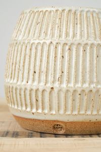 Thrown on the potters wheel of a toasty stoneware clay and finished with a hand carved surface. This versatile container can be used for kitchen storage to potted plants. The planter is finished with a speckled white glaze.