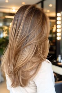 This honey-shaded long hairstyle has soft, sandy highlights that cascade through a blend of expertly cut layers. The depth and structure of the cut give a contemporary feel that's both stylish and timeless. Click here to see more stunning layered haircuts for long hair.