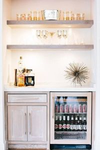 Fantastic bar nook is filled with gray wash floating shelves suspended over gray wash cabinets fitted with a glass front beverage fridge.