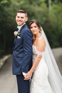 Bride wearing off the shoulder lace wedding dress with cathedral veil in a beautiful up-do with natural glam makeup. Groom wearing Navy suit with white and pink boutonnière. Photo taken at Whistle Bear in Cambridge Ontario by Sandra Monaco Photography.  #WeddingPose #VeilInspiration #CandidPosing #Posing #CouplePose #CandidWedding #Elegant #Romanticposing #PosingInspiration #CouplesPosing #RomanticWedding #WalkingPose #OffShoulderWeddingDress #WeddingDressInspo #WhistleBear