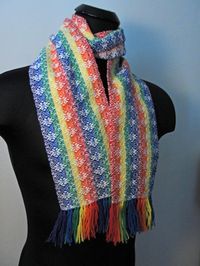 "Hand Woven Wool Rainbow Scarf. Woven in six colors of the rainbow makes for a Unique stand out Scarf. The flower design really pops with the rainbow background. The fringe has been left long for you to shorten as you desire. This piece measures approximately 68.5\" long (fringe end to fringe end) and 6.25\" wide."