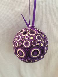 2 1/2 foam ball covered in paper quilled design, sprayed with paper sealer. Colors are two different purples, cream with a purple ribbon to hang it.