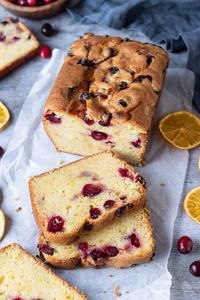 Vegan orange cranberry cake on a sheet of white baking parchment with dried orange slices and fresh cranberries.