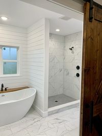 Walk in marble tile shower, soaking tub, shiplap walls, stained wood barn door