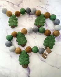 This tree felt garland invokes the serenity of the outdoors without all the mosquitos!The garland is comprised of 5 trees with colorful corresponding felt balls. It would be perfect for a nature-themed nursery, bedroom, fireplace, bookshelf or a woodland party! Felt ball garland is a versatile, reusable, and eco-friendly decoration that adds a beautiful touch to any environment or occasion!Colors: Trees (5) + Powdered Blue (5) + Beige (5) + Peppercorn (5) + Forest (5) + Gray (5) = total of 30 fe