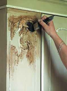 a person with a brush painting the side of a cabinet