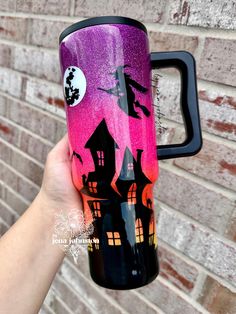 a person holding up a purple and black travel mug with witch silhouettes on it