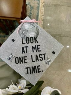 a graduation cap with the words look at me one last time on it and flowers