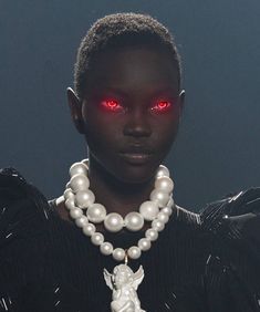 a woman with red eyes and white beads on her neck, standing in front of a dark background