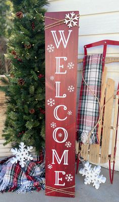 a wooden welcome sign sitting next to a christmas tree and sled with snowflakes