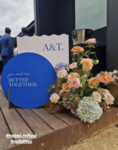 a blue sign sitting on top of a wooden table next to flowers and vases