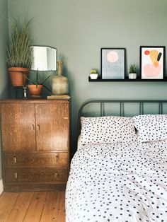 a bed sitting next to a wooden dresser in a room with two pictures on the wall