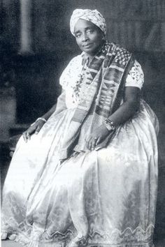 an old black and white photo of a woman in a dress sitting on a chair