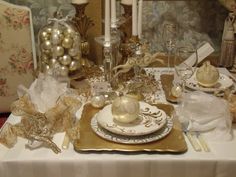 the table is set with gold and white dishes, silver candlesticks, and ornaments