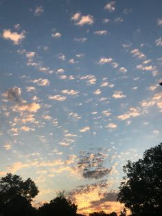 the sky is filled with clouds as the sun sets in the distance behind some trees