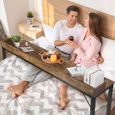 a man and woman sitting on top of a bed next to a tray with donuts