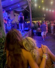 two women hugging each other in front of a crowd at an outdoor concert with lights on