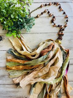 a necklace with beads and leaves on it sitting on a table next to a plant