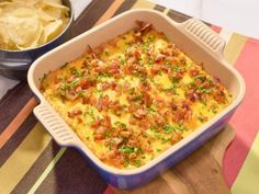 a casserole dish with bacon, cheese and green onions next to a bowl of potato chips