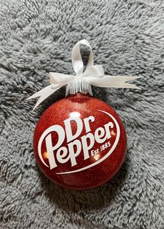 a dr pepper ornament hanging from a white ribbon on top of a gray carpet