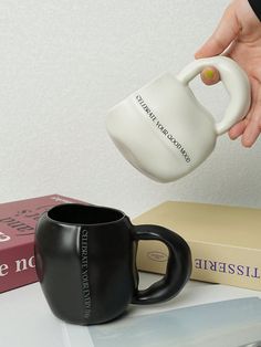 a person is pouring coffee into a black and white mug on a table next to books