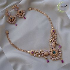 a gold necklace and earring set with multi colored stones on a white satin background